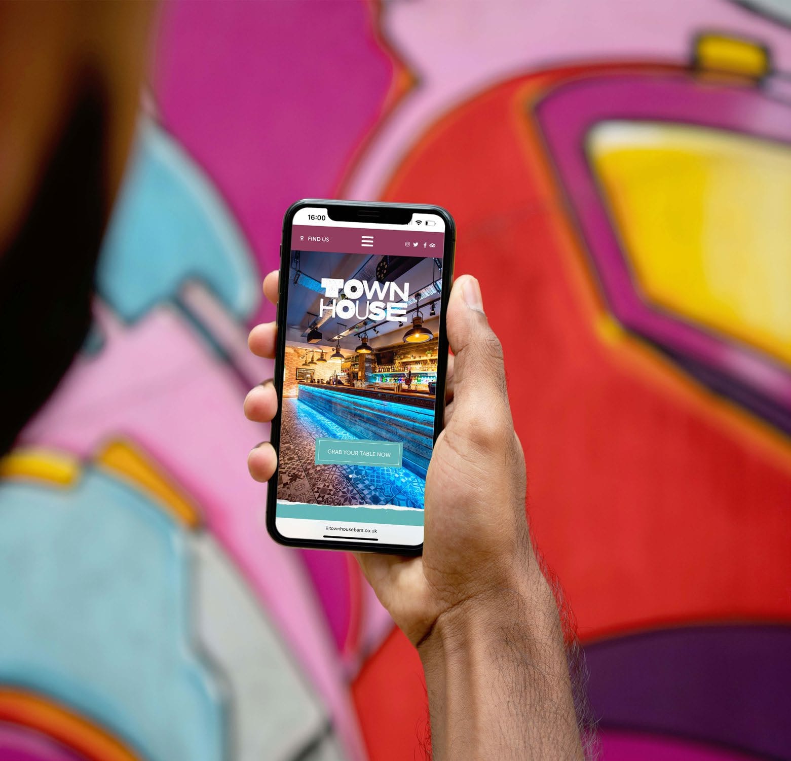 The TownHouse website on a phone held against a graffiti wall