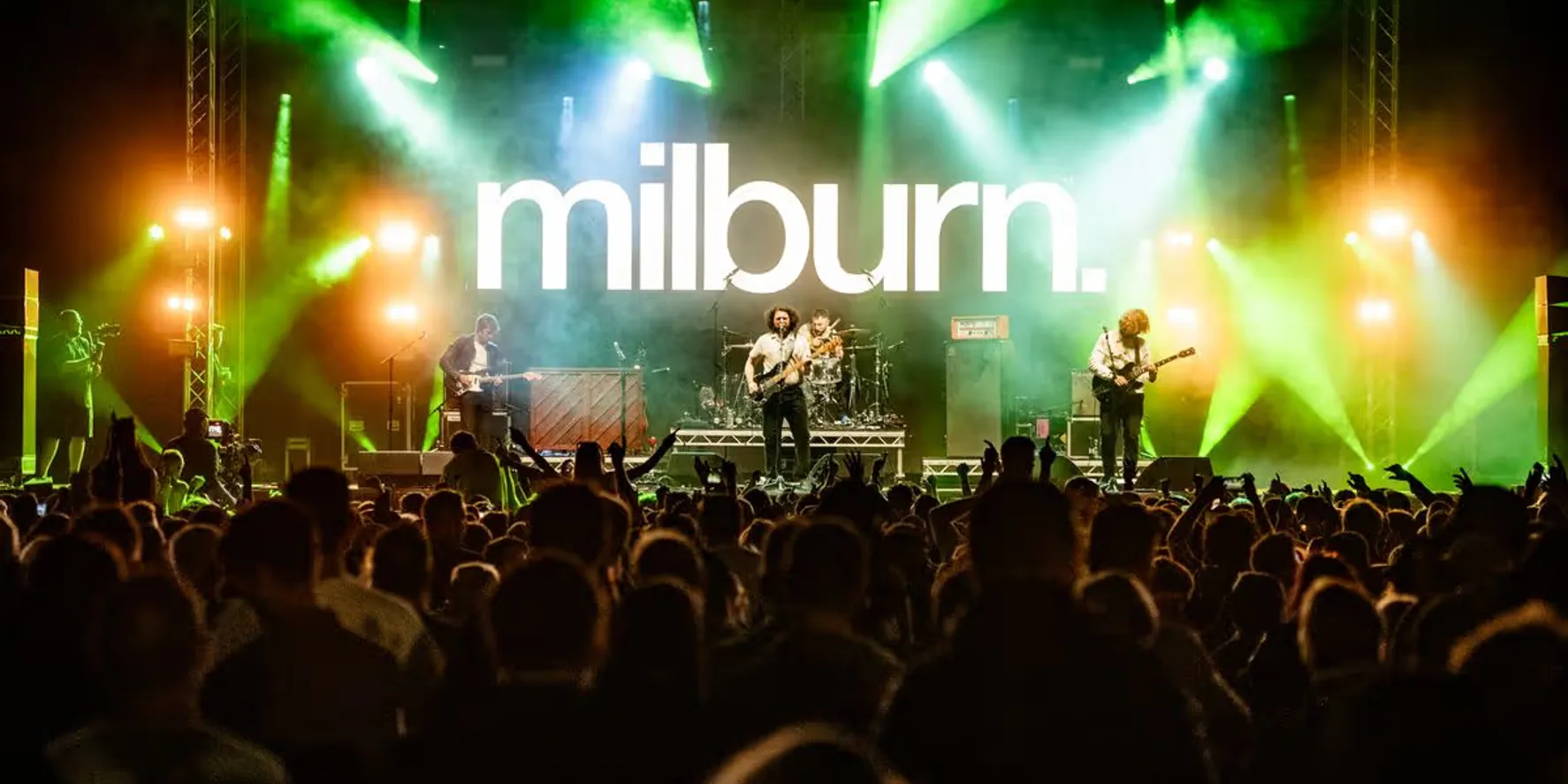 A packed festival crowd facing the main stage in green and orange lights at Rock N Roll Circus.