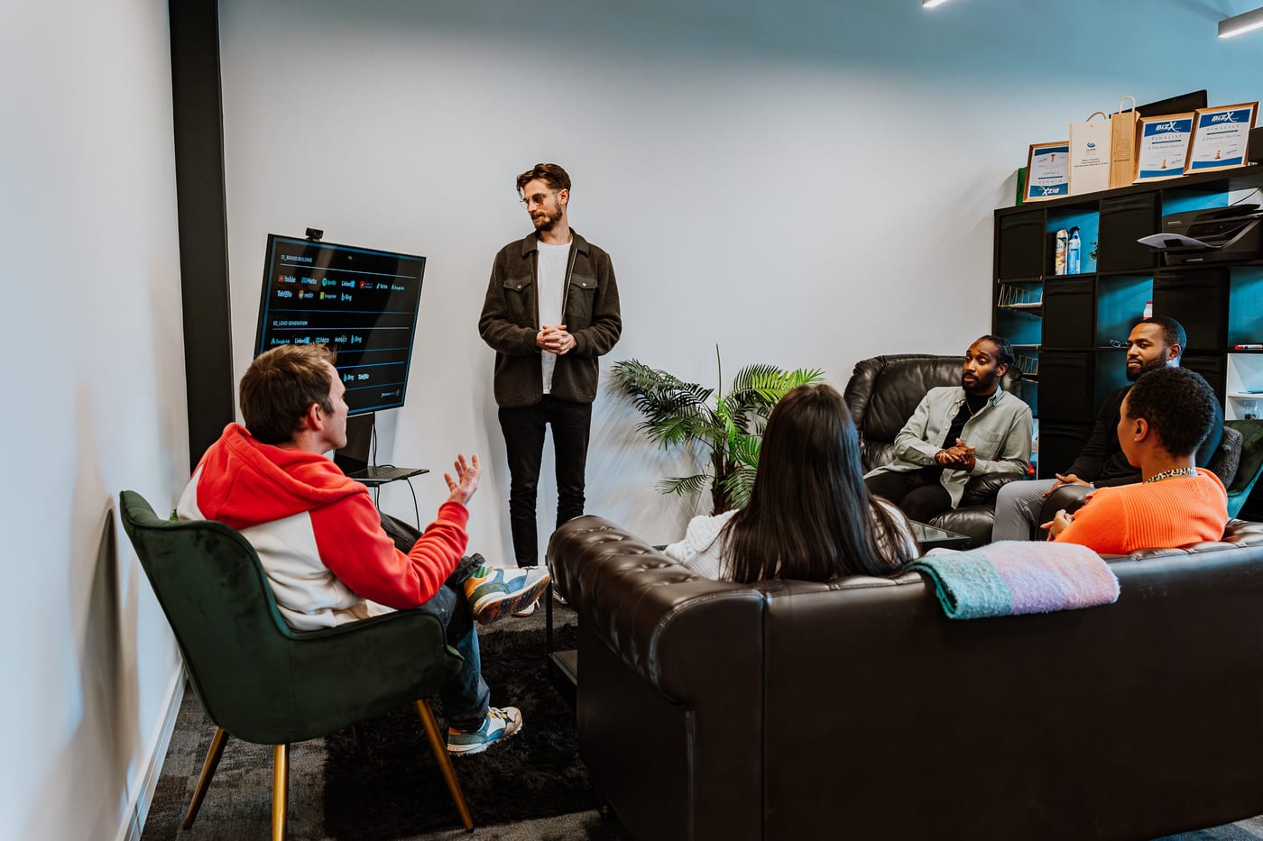 A 21 Degrees team member presenting to colleagues gathered on sofas around a screen in the office lounge.