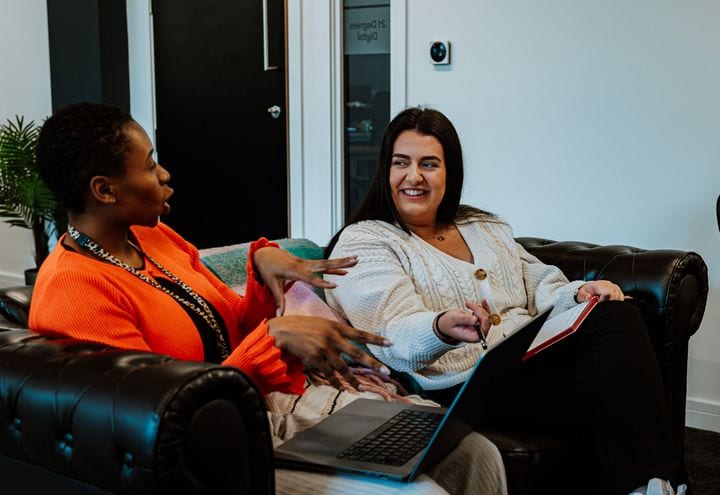 Two 21 Degrees colleagues chatting on the studio sofa.