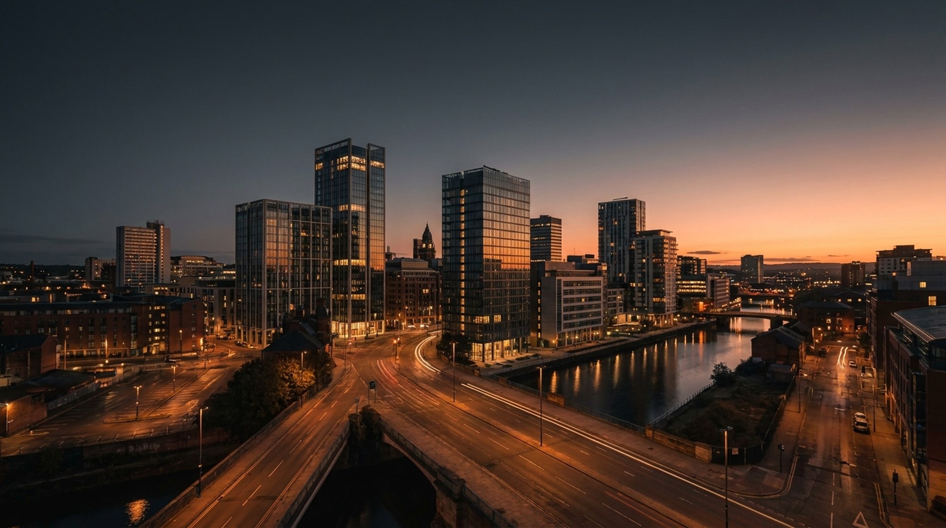 The Leeds skyline at dusk, glass riverside towers lit under an orange sunset sky.