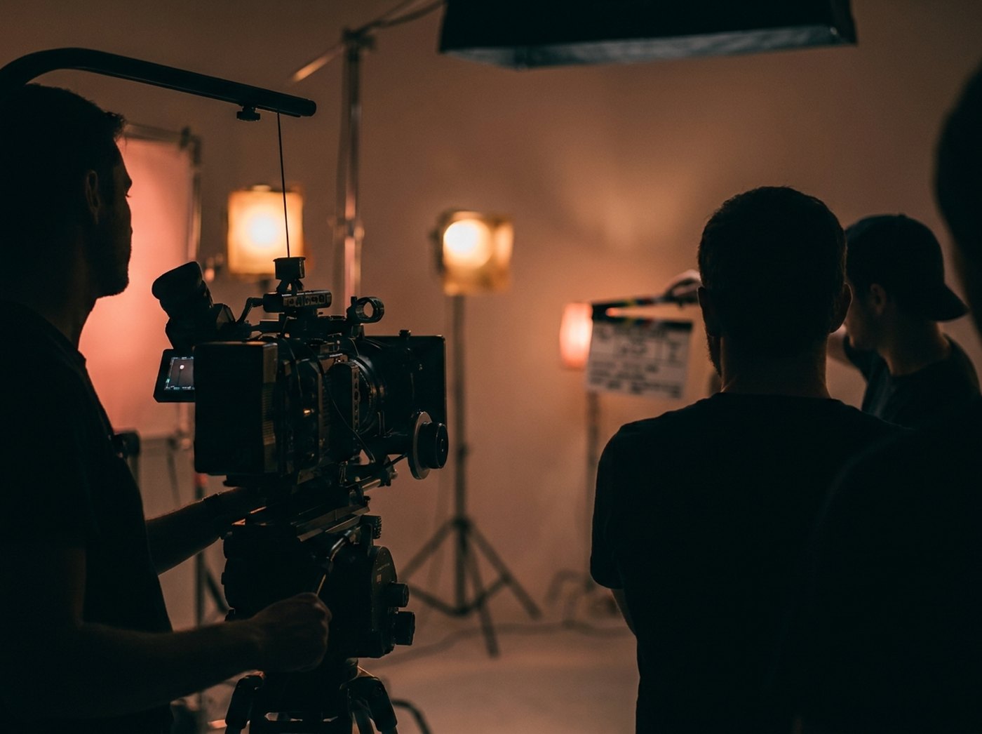 A film crew lining up a cinema-camera shot on a warm-lit studio set.
