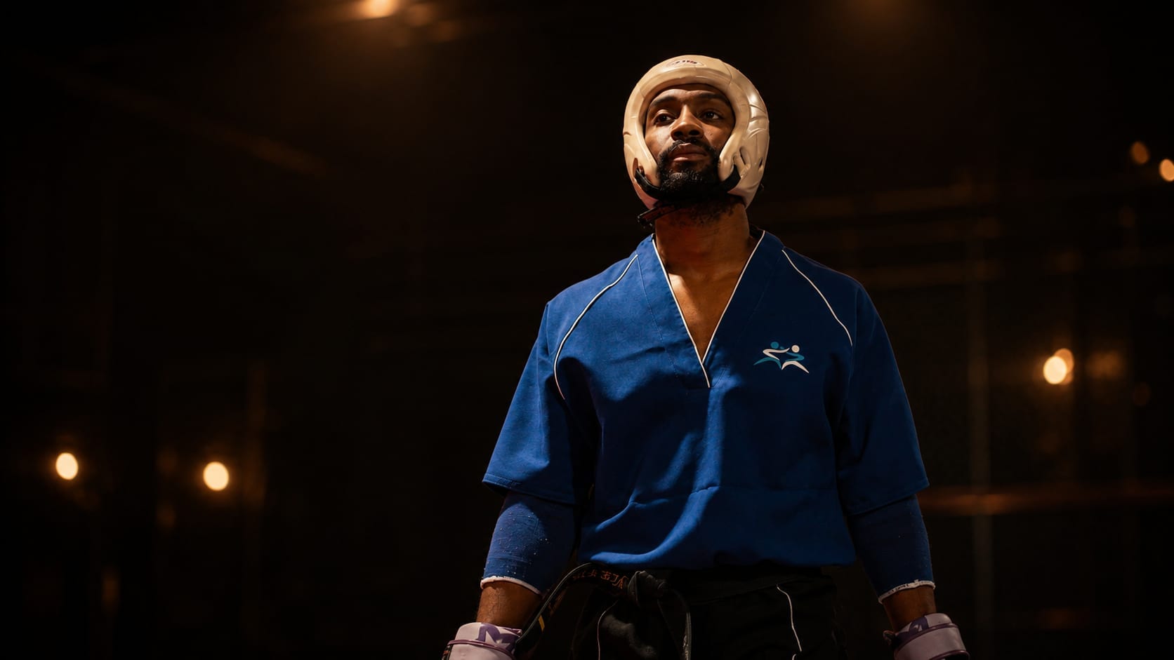 Kyle Findley in taekwondo sparring kit and headguard, standing in a training hall under warm light.