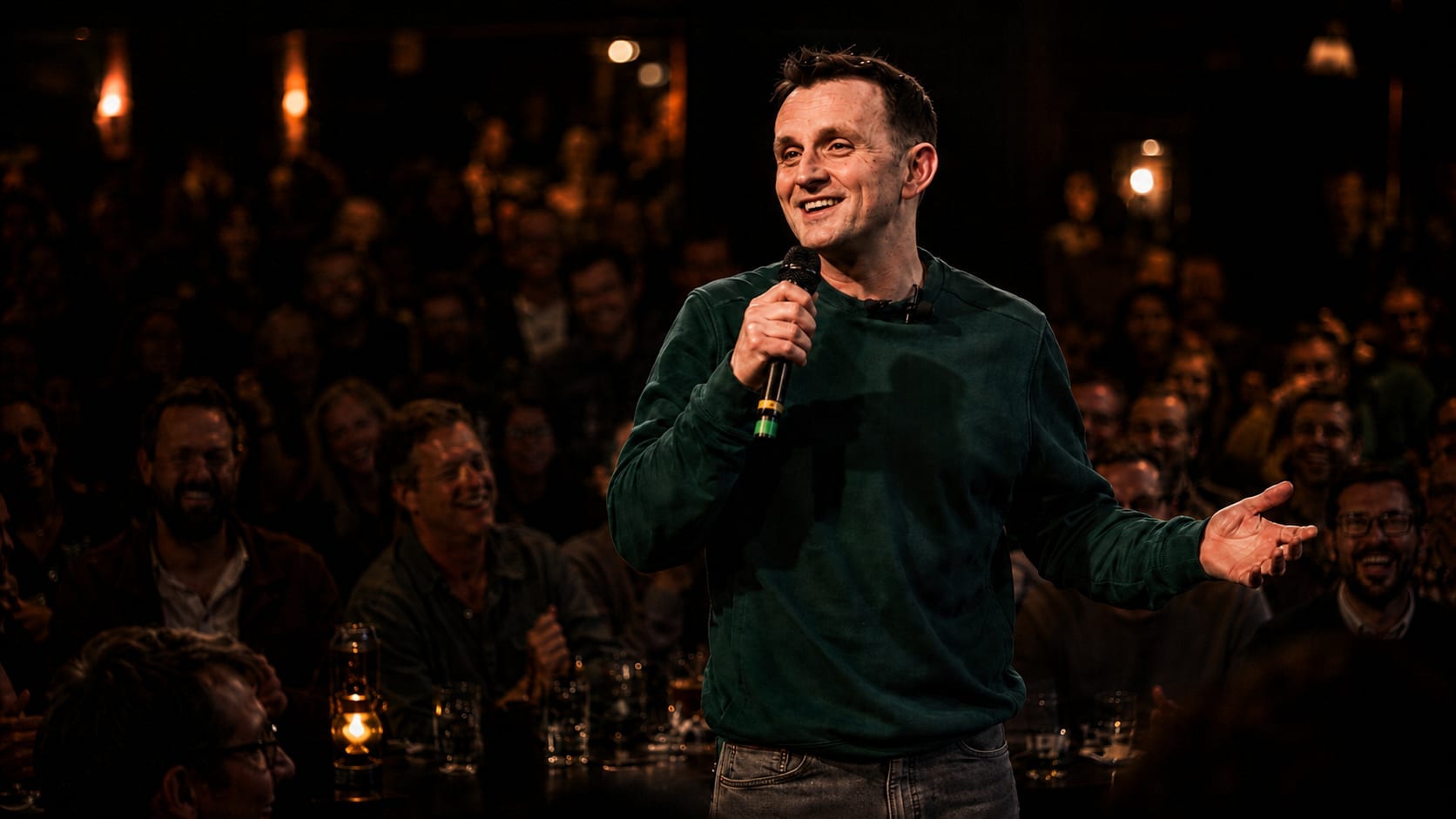 Rory Mason performing stand-up comedy with a microphone in front of a live audience under warm stage lighting.