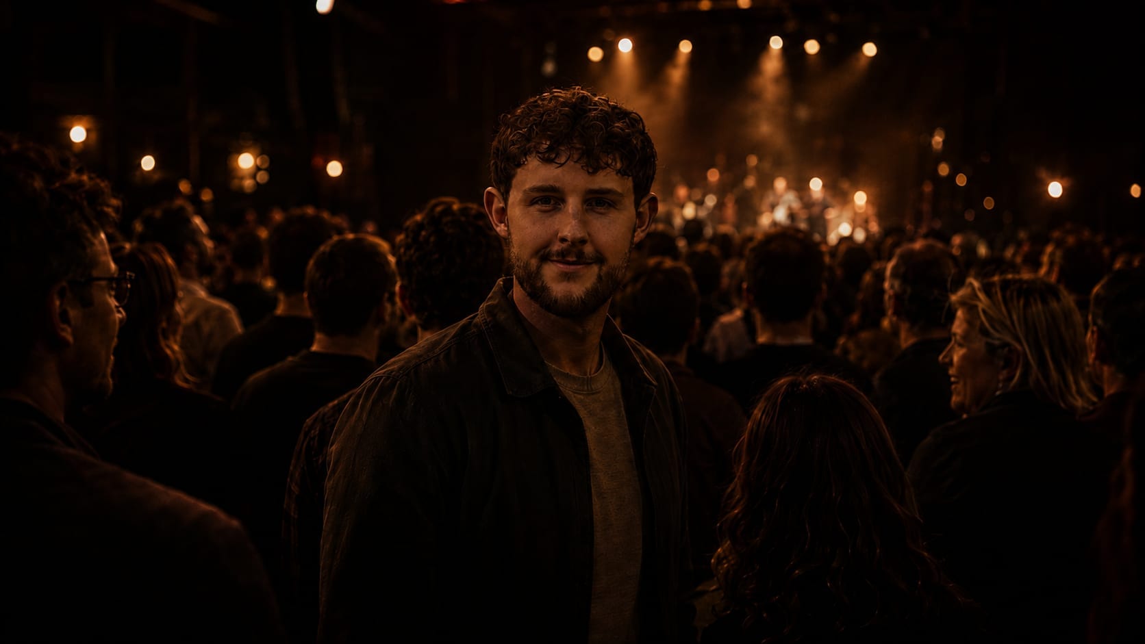 Seth Leech standing in the crowd at a live gig with a band performing on the lit stage behind him.